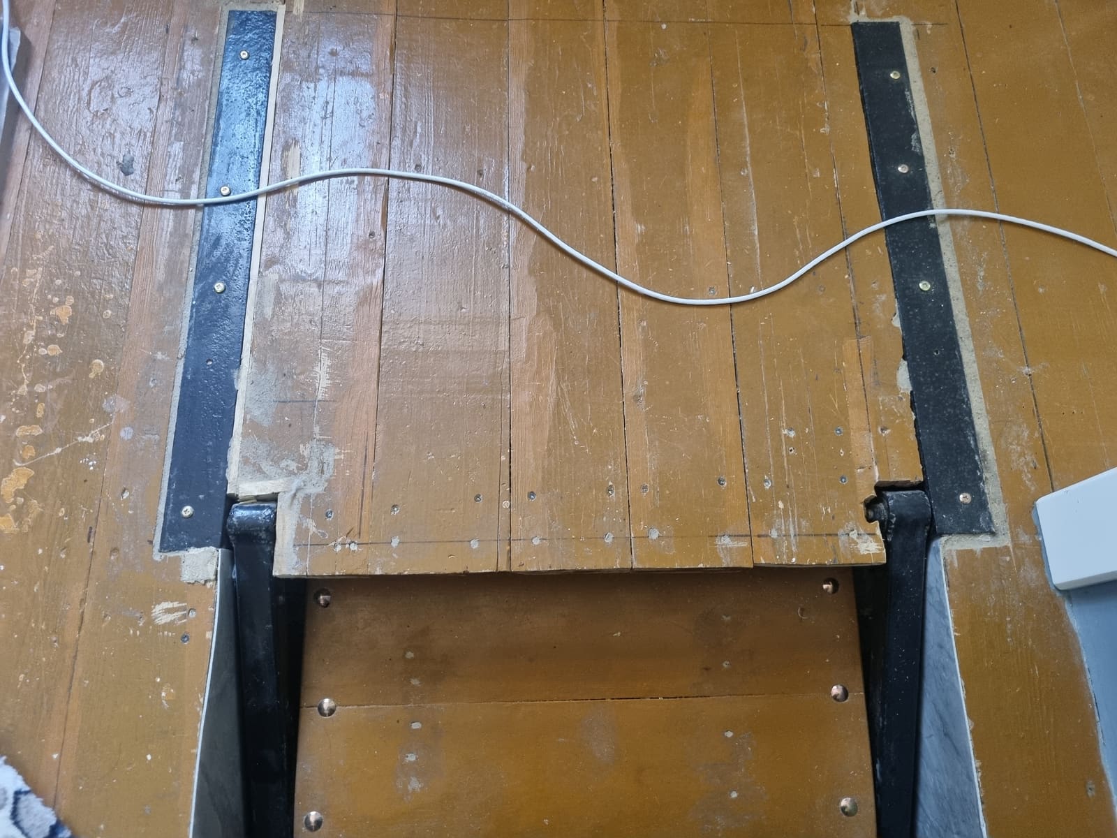 Detail of the black steel rails recessed flush into the wooden floor at the pivot end